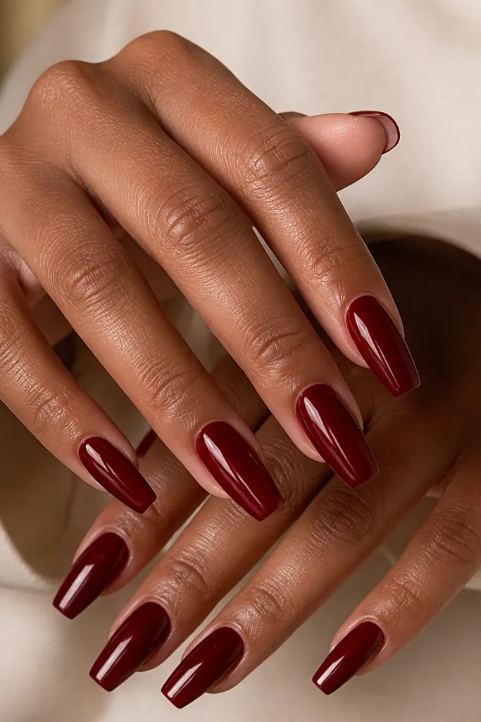 A set of coffin-shaped acrylic nails in deep cherry red. The cuticle area is clean and even, with a glossy top coat that reflects a sharp highlight line. Nails are medium length, tapered to a squared tip.