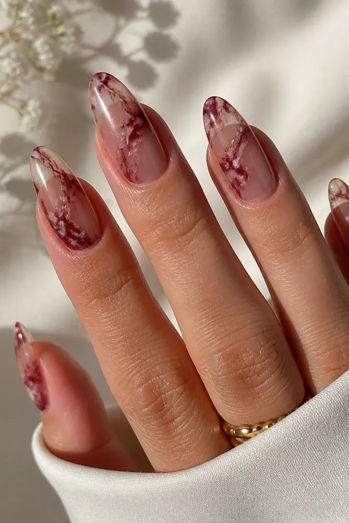 Almond nails with a translucent clear base and dark cherry red marble veining. Thin white-ish streaks sit under the red veins for a marbled stone effect. The top coat is glossy.