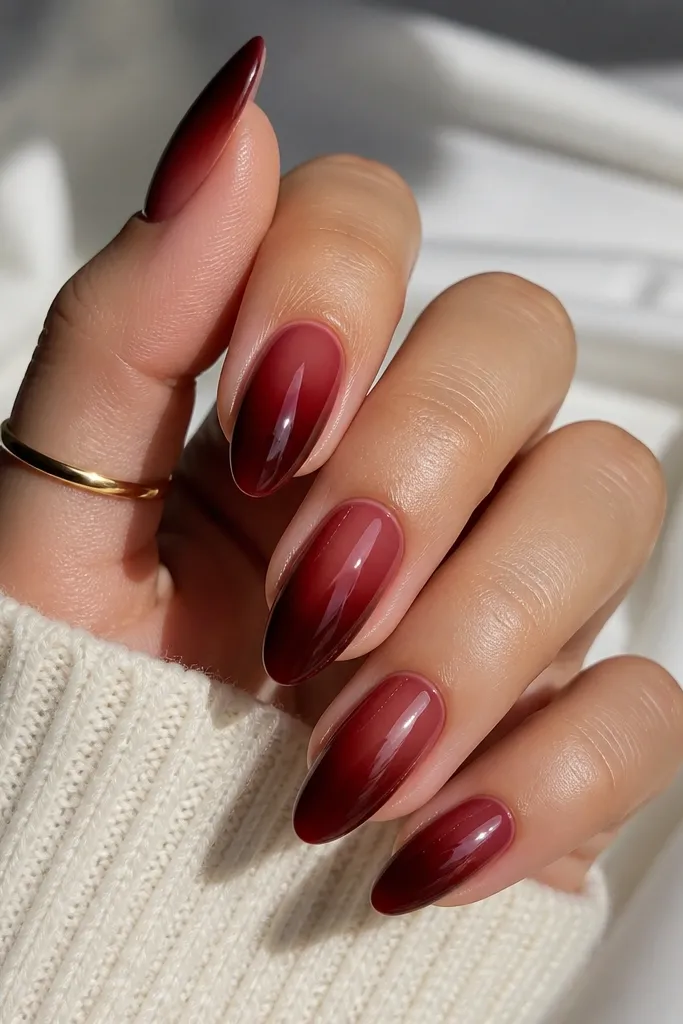 Almond nails where dark cherry red fades outward from the cuticle like a soft aura. The center near the cuticle is slightly lighter and blends into deeper red toward the tip. Glossy top coat.