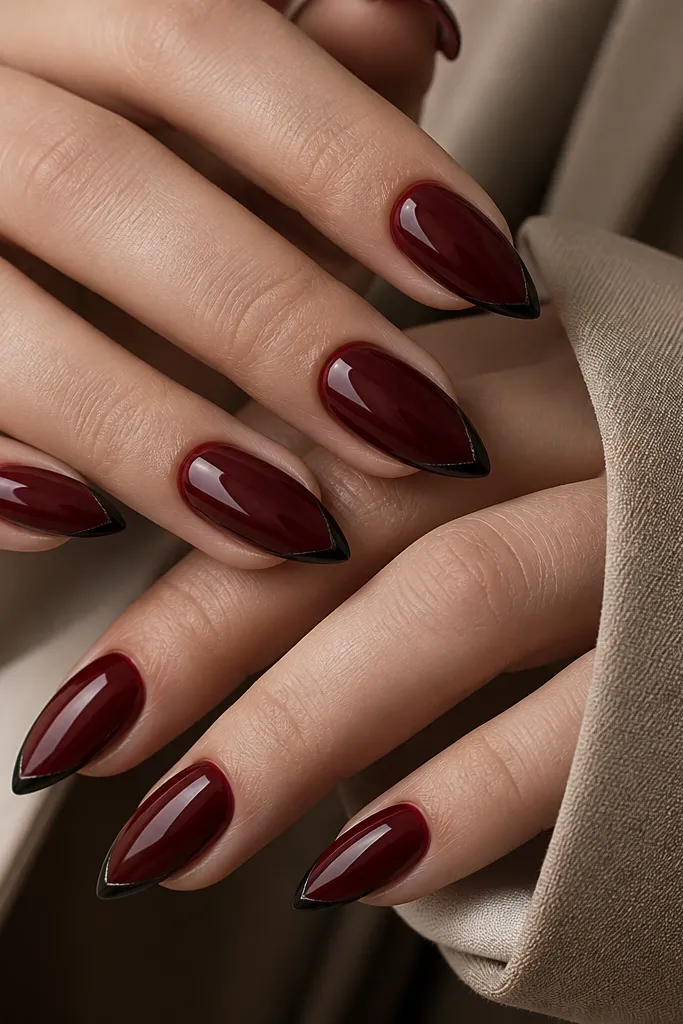 Dark cherry red nails with a super thin micro-French line near the tips, and a small black V shape centered at the very end, sharp almond tips.