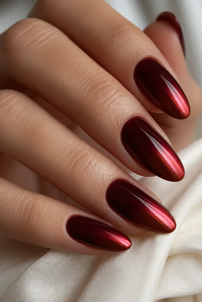 Dark cherry red nails with a smooth ombré fade into red chrome at the tips, almond nails, mirror-like shine.