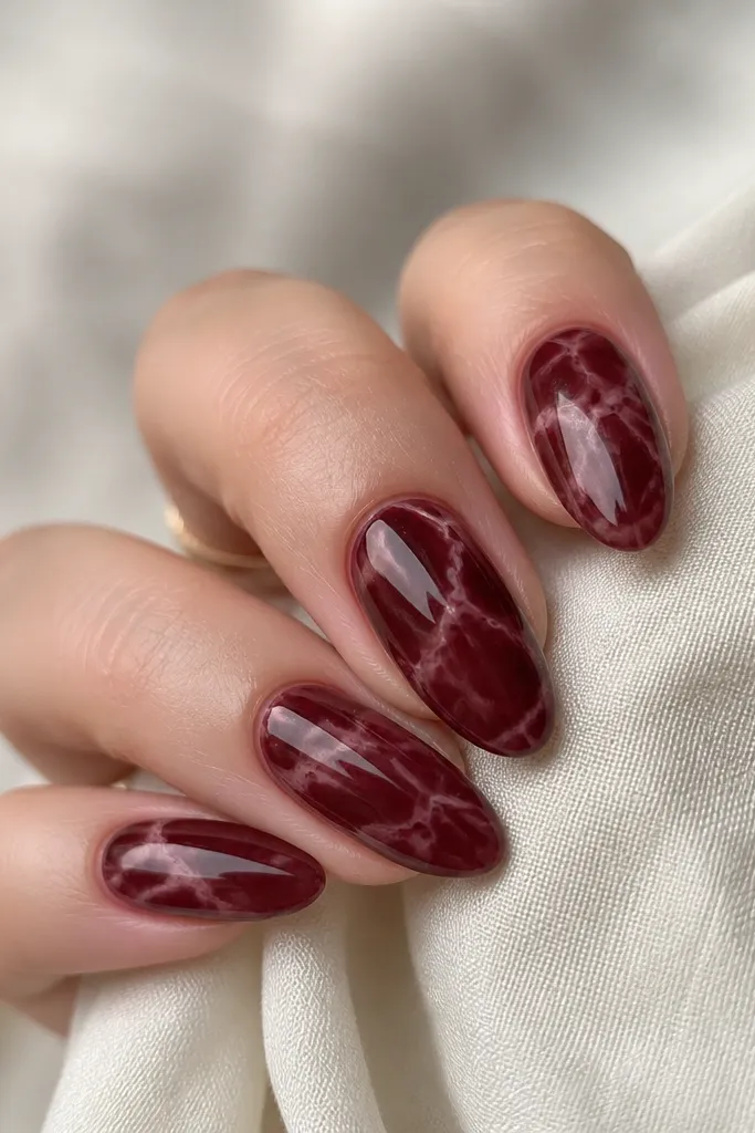 Dark cherry red marble nails with thin nude and light-pink veining swirls, glossy, almond shape.
