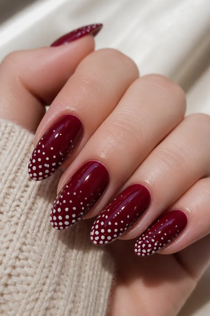Dark cherry red nails with a gradient of small white dots that get larger toward the tip, glossy almond nails.