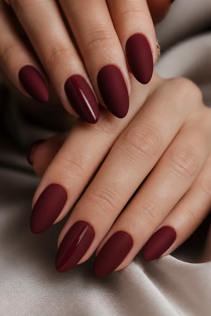 Medium length almond nails in dark cherry red with a velvety matte finish. On two accent nails, there is a single narrow glossy vertical stripe in the center, catching light even though the rest is matte.
