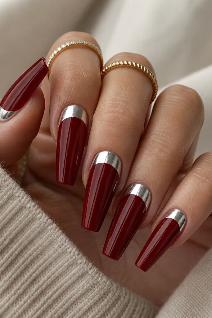 Long coffin nails painted deep cherry red. The lower half-moon near the cuticle is covered in silver chrome foil, leaving the rest of the nail glossy cherry. The chrome has a smooth, reflective crescent shape.