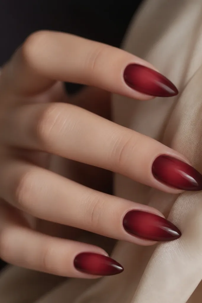 Almond nails with a dark cherry red base. The center of each nail has a soft, airbrushed aura glow that fades outward, creating a halo effect in a slightly lighter cherry tone.