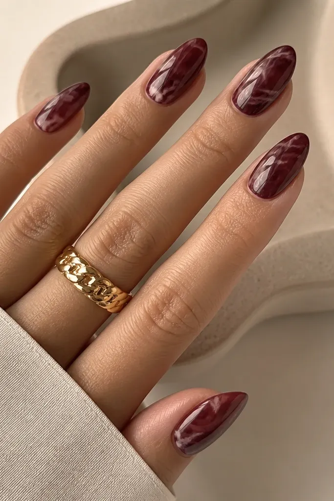 Medium almond nails with dark cherry red marble pattern. Thin blush nude veins run through the cherry, creating a marbled look like stone. The finish is glossy and smooth.