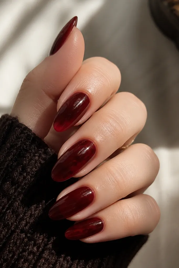 Almond nails painted with a translucent jelly dark cherry red that glows under light. The nails have a glossy, gel-like shine and show slight depth through the color.