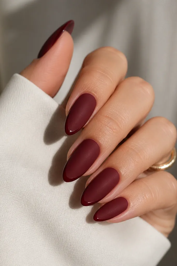 Almond nails in dark cherry with a velvet matte finish. The very tip edge has a thin glossy outline that catches light, creating a subtle frame.
