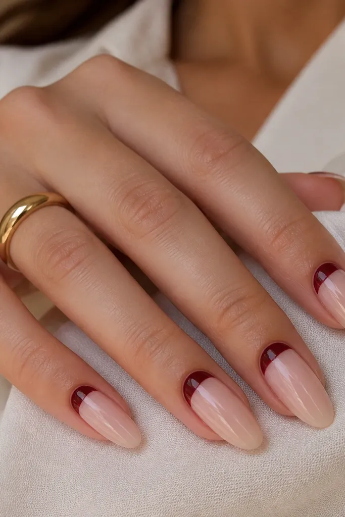 Almond nails with a sheer nude base and a dark cherry half-moon shape at the cuticle. The rest of the nail is nude and glossy.