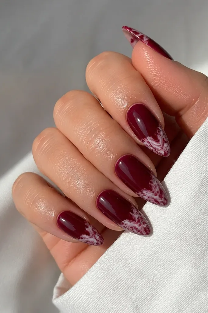 Almond nails with solid dark cherry base and marble swirls only on the tips. The swirls are milky white and deep burgundy, concentrated at the free edge.