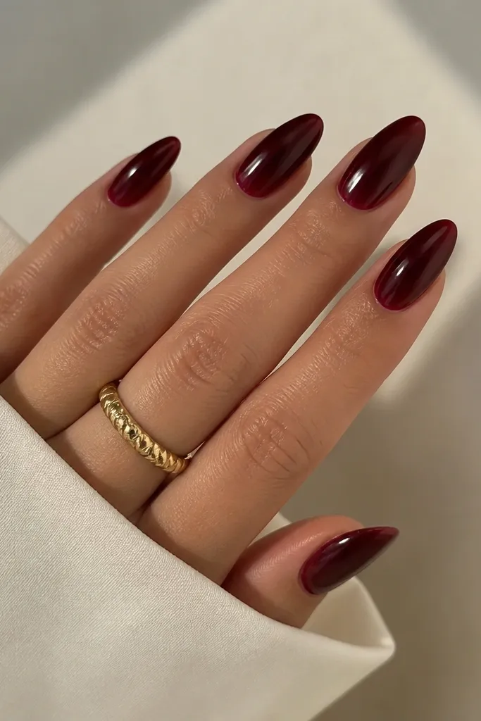 Almond nails in dark cherry red with a slightly lighter bevel line along each sidewall near the middle, like a shadowed contour. The rest is glossy and even.