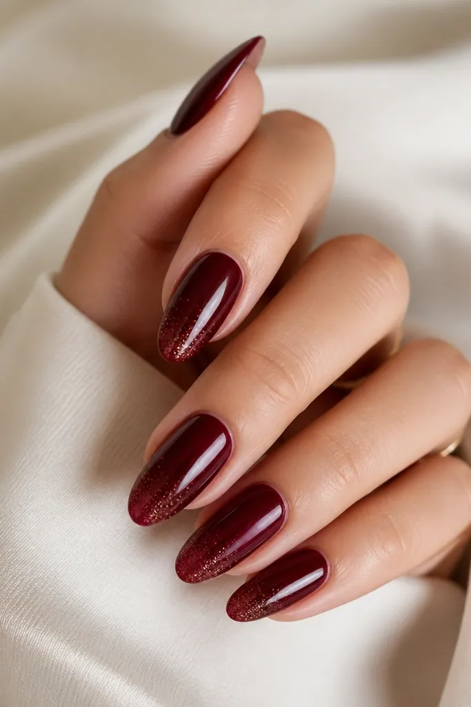 Almond nails in dark cherry red with a fine micro-glitter dust concentrated only at the free edge. The glitter fades out toward the middle.