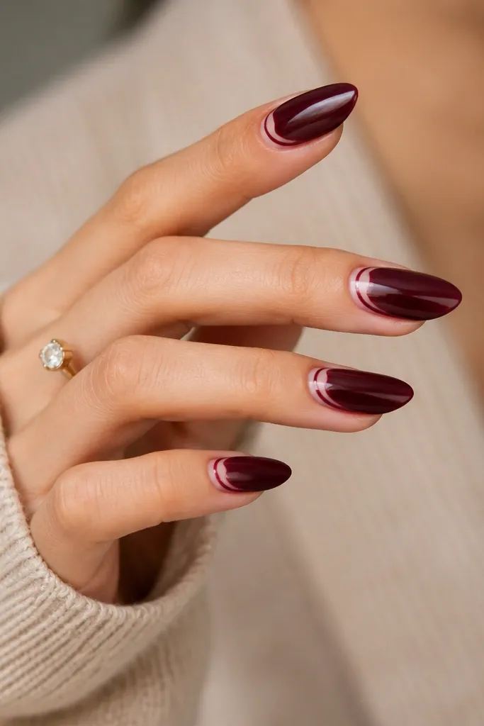 Dark cherry red nails with two thin metallic lines near the cuticle: one line in gold and one line in silver, forming a narrow double accent. The lines are straight and clean.