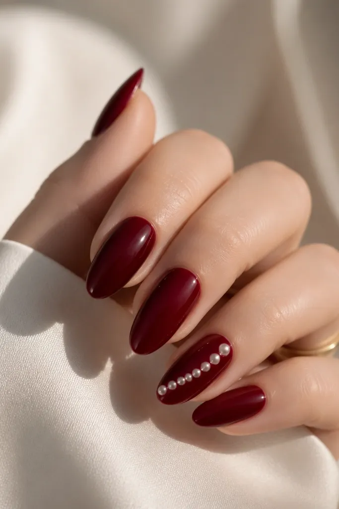 Almond nails in dark cherry red with a trail of small pearlized dots running diagonally from mid-nail toward the tip on one accent nail. The dots look like tiny beads under glossy top coat.