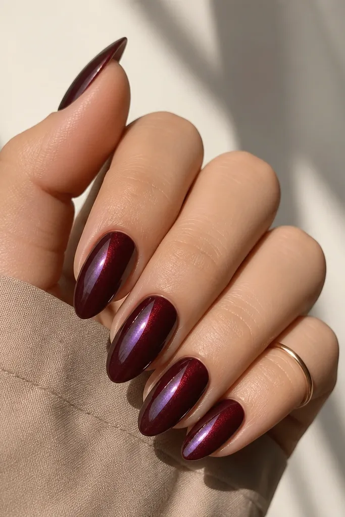 Almond nails painted dark cherry red with a color-shift wine top coat that flashes slightly purple and brown under different angles. The finish is glossy and smooth.
