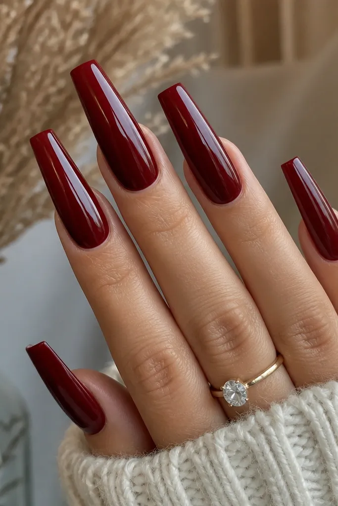 Long coffin nails painted a deep wine-red cherry color, fully opaque and mirror-glossy, with crisp edges and a smooth reflective shine across all nails.