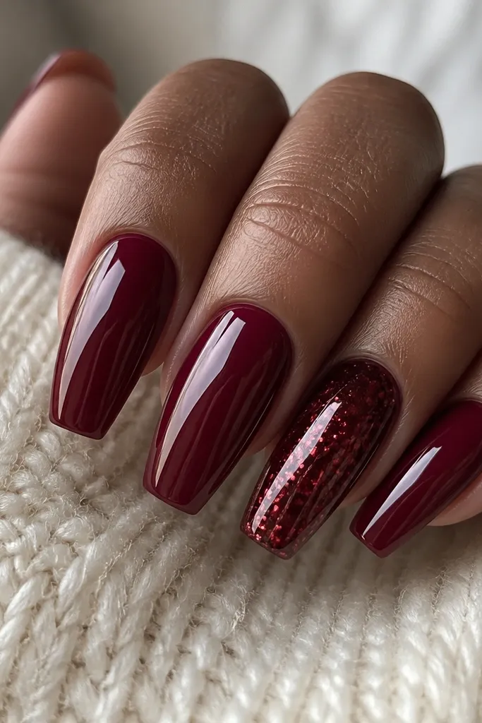 Four nails painted glossy dark cherry red; one accent nail has cherry-red chrome flakes across the coffin tip with a metallic sheen.