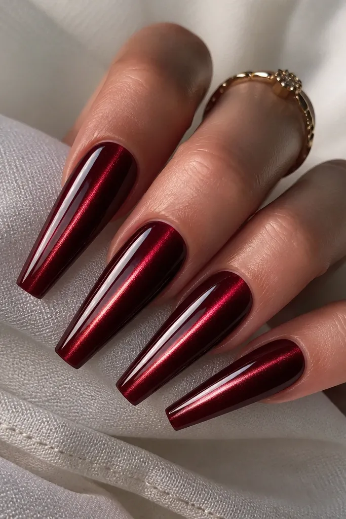 Coffin nails in dark cherry red with a magnetic cat-eye line running vertically down the center, glossy and reflective like a gemstone.