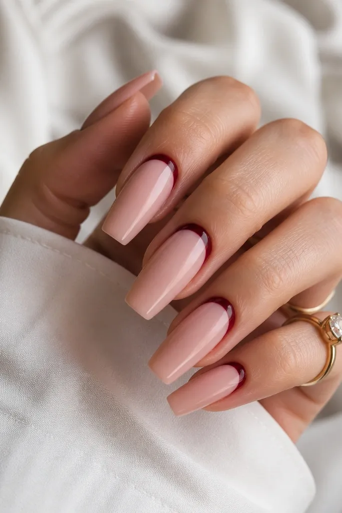 Coffin nails with a nude pink base; the cuticle area has a dark cherry red reverse French arc that stops short of the sidewalls, glossy overall.