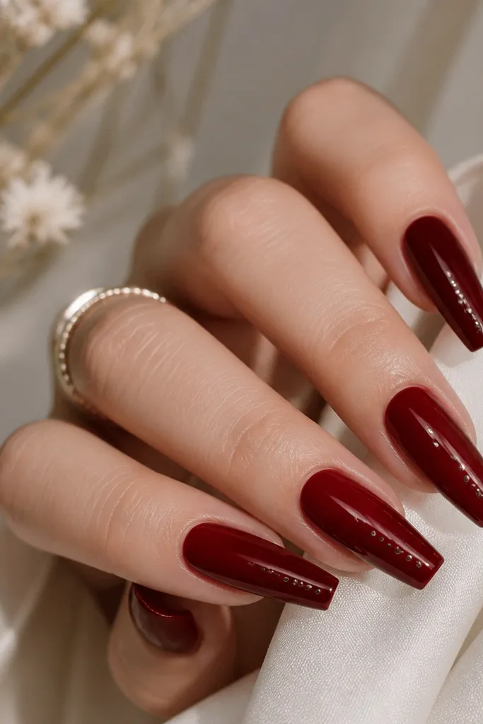 Coffin nails in glossy dark cherry red with tiny metallic studs lined along one side near the middle and toward the tip.