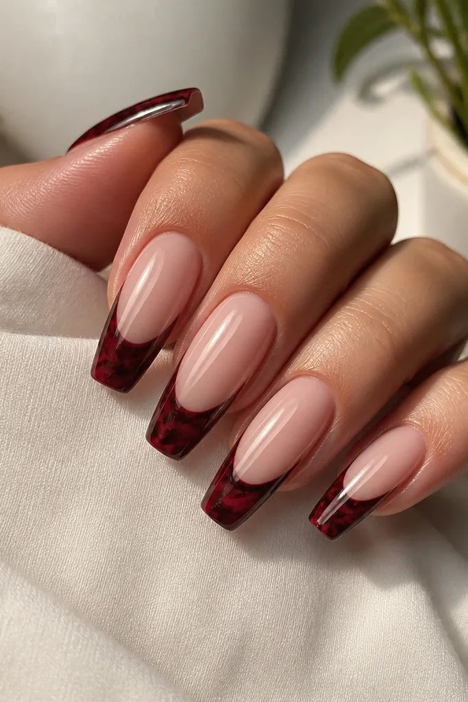 Coffin nails with a nude base; French tips are marbled in dark cherry red with black swirls, glossy finish.
