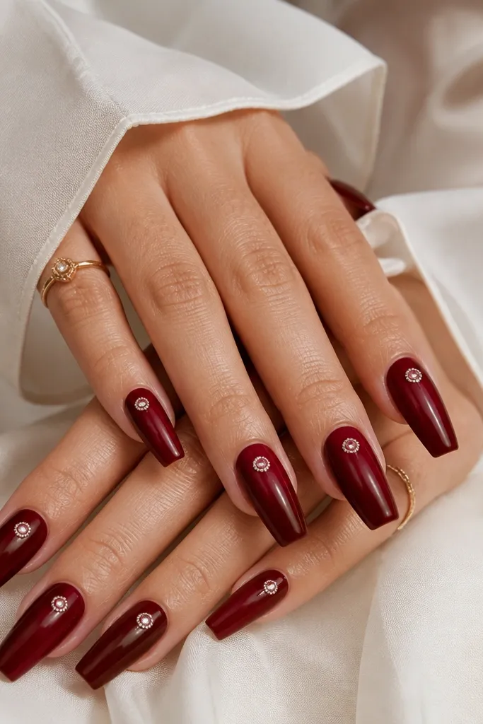 Coffin nails glossy dark cherry red with a small halo of tiny crystals around a single point near the center of each nail, giving a subtle sparkle.