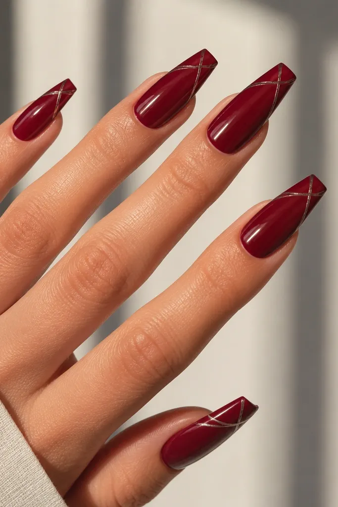 Coffin nails painted glossy dark cherry red with thin silver line art drawn in a diagonal arc near the tip, minimal and crisp.