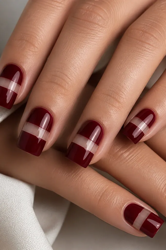 Square nails with dark cherry red base; a nude sheer stripe runs horizontally across the nail near the middle, creating a backwards French look, glossy finish.