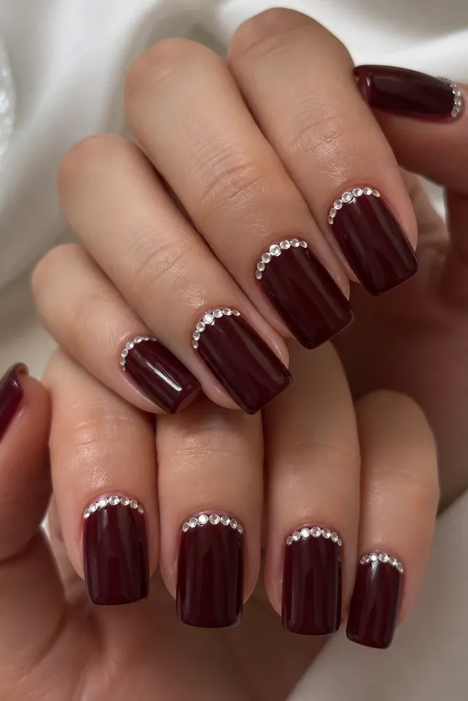 Square dark cherry nails with a thin line of small rhinestones starting at one side of the cuticle and stopping near the other, glossy base.