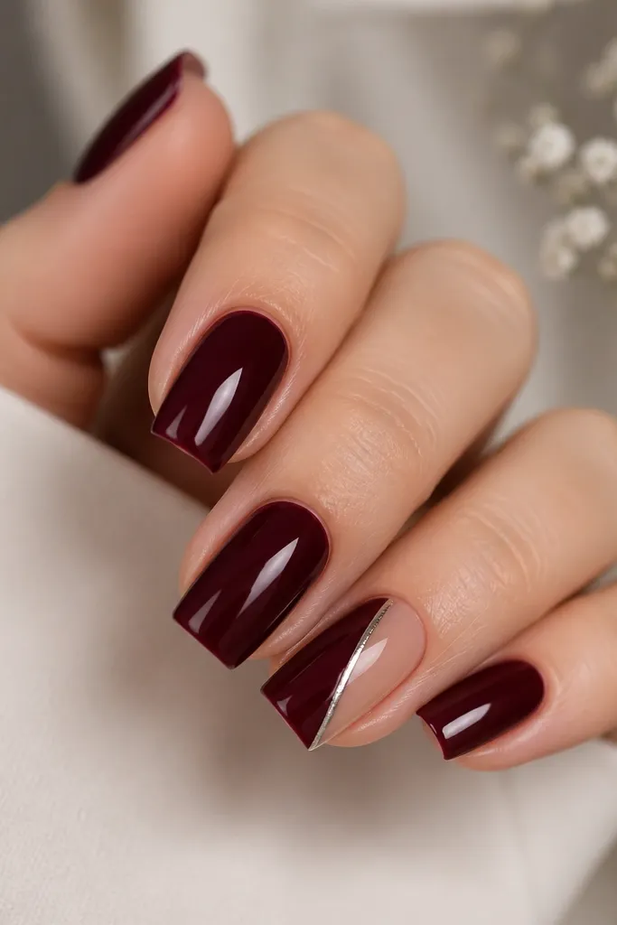 Square dark cherry nails with a clean diagonal or side-slit negative space panel on one nail, outlined by a thin silver line, glossy rest.