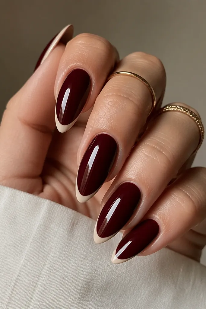 Almond nails painted deep dark cherry red on the full nail with a crisp French tip in creamy nude. The smile line is thin and slightly curved, with a high-gloss top coat reflecting light.