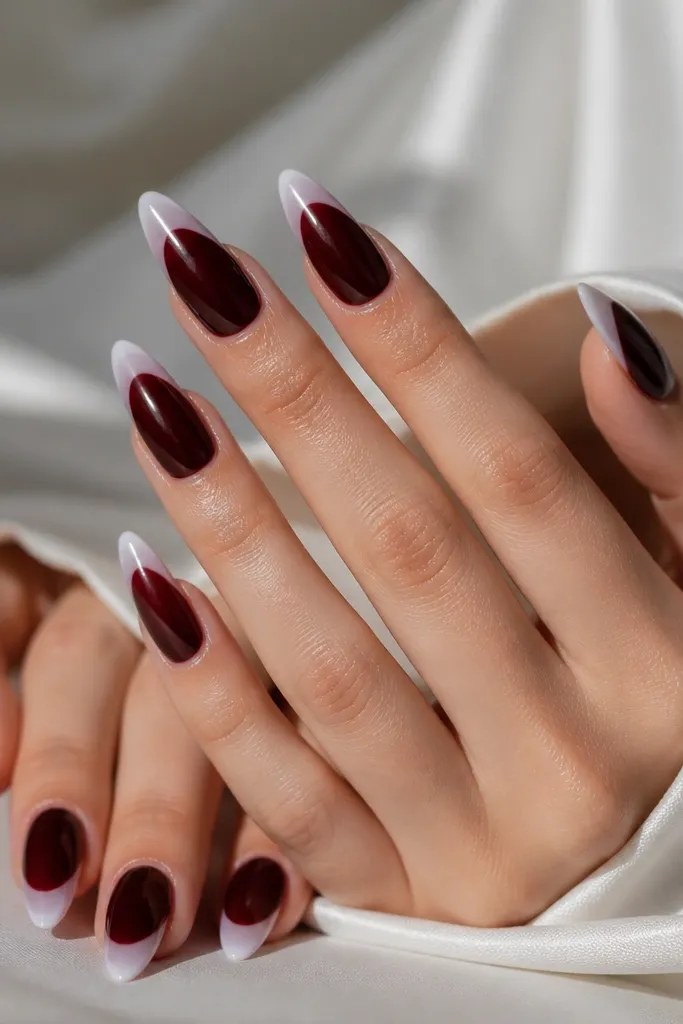 Almond nails with a glossy dark cherry base and a milky white French tip. The white tip is semi-opaque with a soft edge, and the nails reflect highlights under direct light.