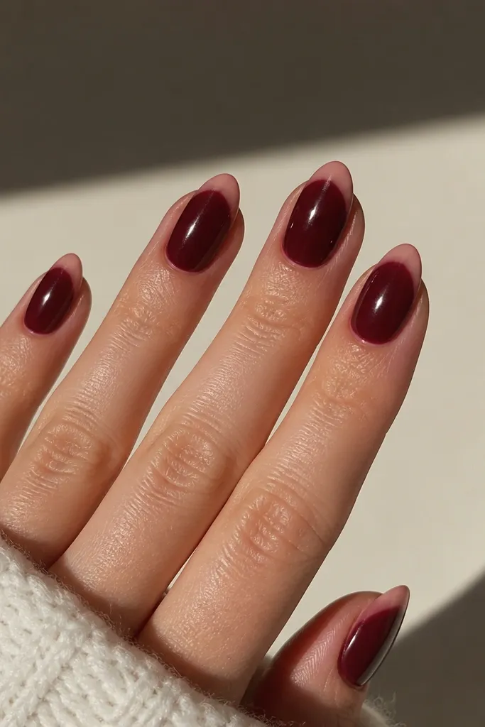 Almond nails show a dark cherry red base with a barely-there rosy nude French tip. The tip is translucent and the shine makes it look like the nail is naturally rimmed.