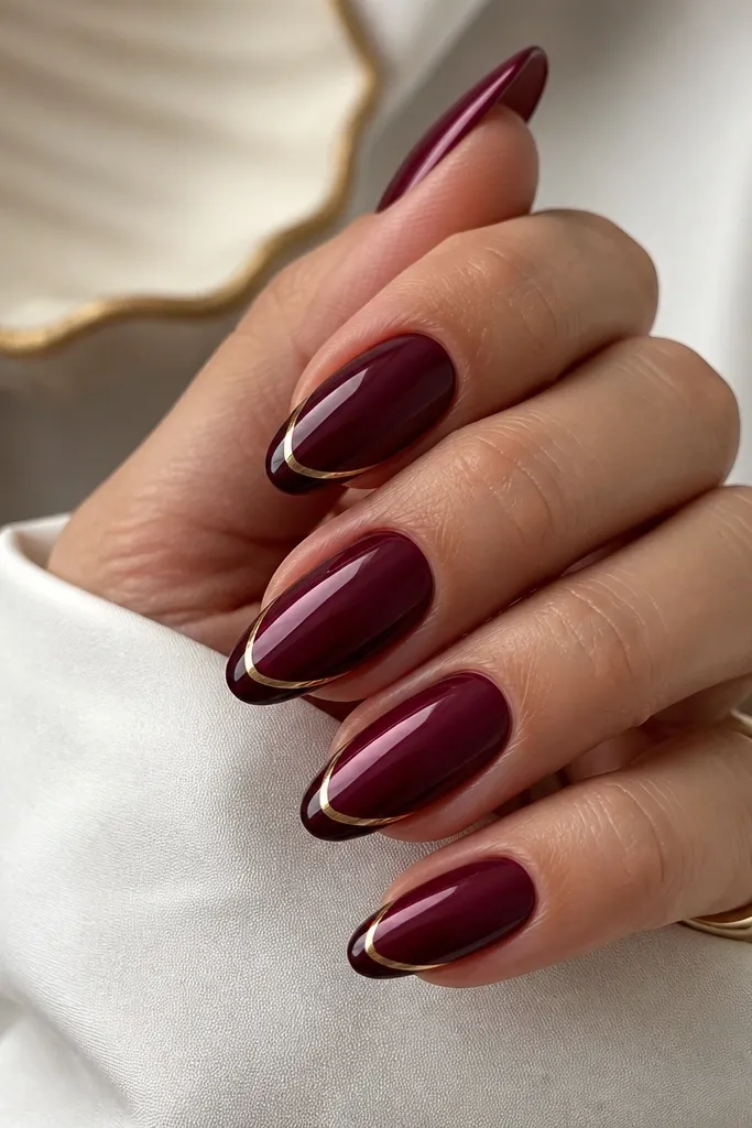 Almond nails in dark cherry red with a French tip filled in glossy dark cherry. A single thin gold line outlines the smile line, like a gold marker tracing the tip edge.