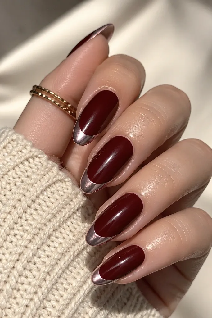 Almond nails in dark cherry red with a French tip finished in icy nude chrome. The chrome looks like pale silver with a rosy undertone, reflecting light sharply against the cherry base.