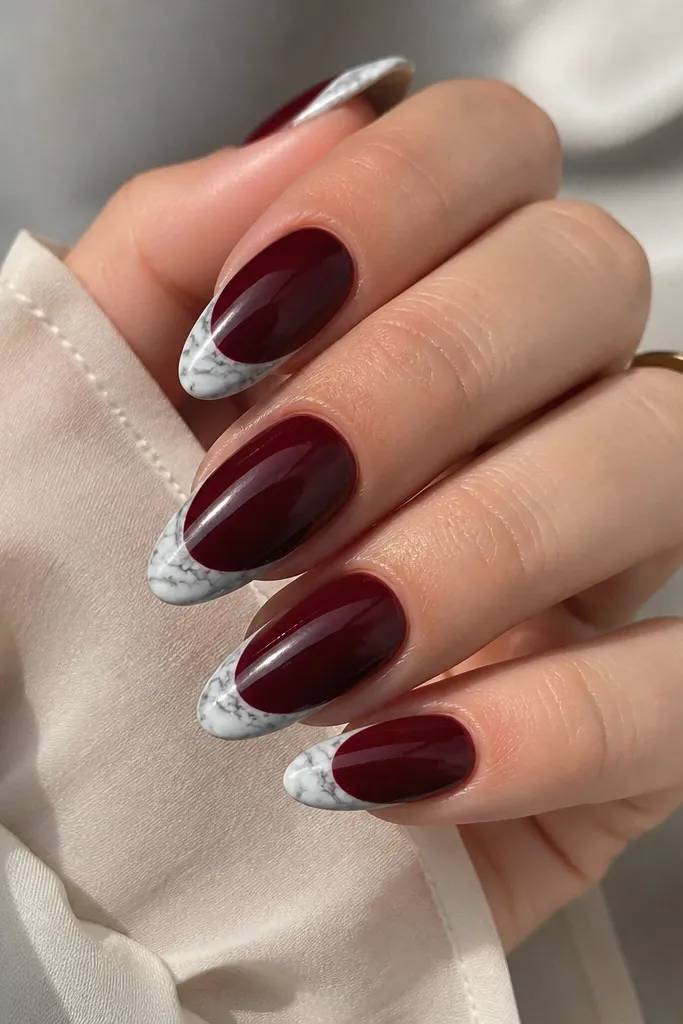Almond nails with dark cherry base and a French tip that looks like white marble. Thin gray-white veining runs through the tip, with a glossy top coat that makes the marble look glassy.