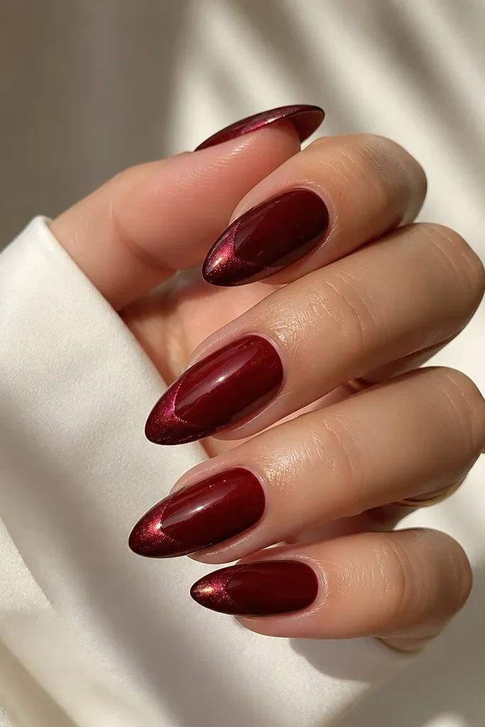 Almond nails with dark cherry red base. The French tip has a black cat-eye chrome line that shifts in light, forming a thin magnetic streak near the smile line.