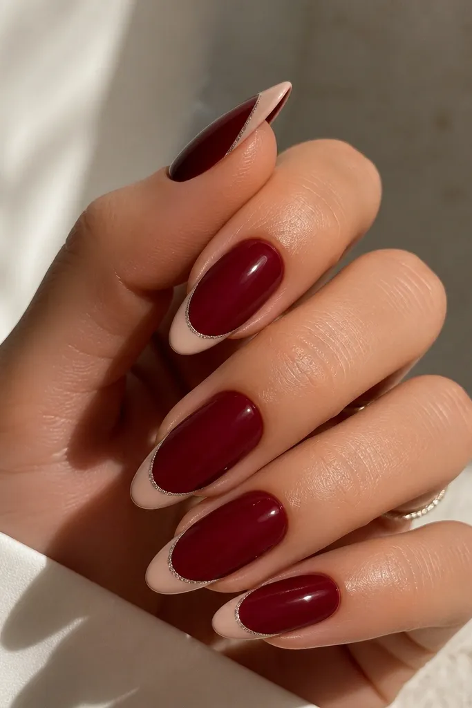 Almond nails in dark cherry red with a classic nude French tip. At the very outer edge of the tip, there's a dusting of fine silver shimmer, leaving the inner tip clean.