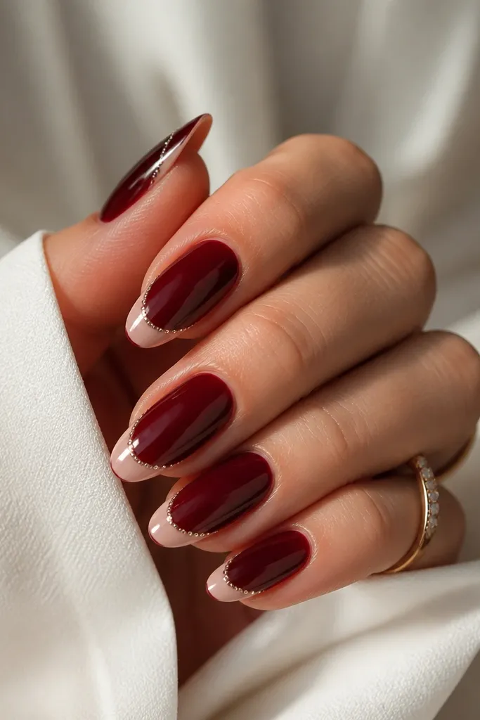 Almond nails in dark cherry red with a classic nude French tip. Along the smile line, tiny clear crystal dots are spaced evenly like a delicate border.