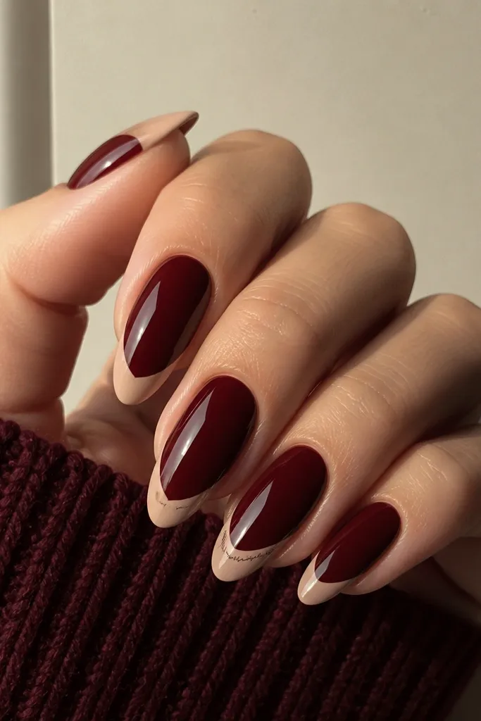 Almond nails with dark cherry red base and a nude French tip. On one nail (ring finger), tiny black micro-lettering runs along the smile line like a short signature.