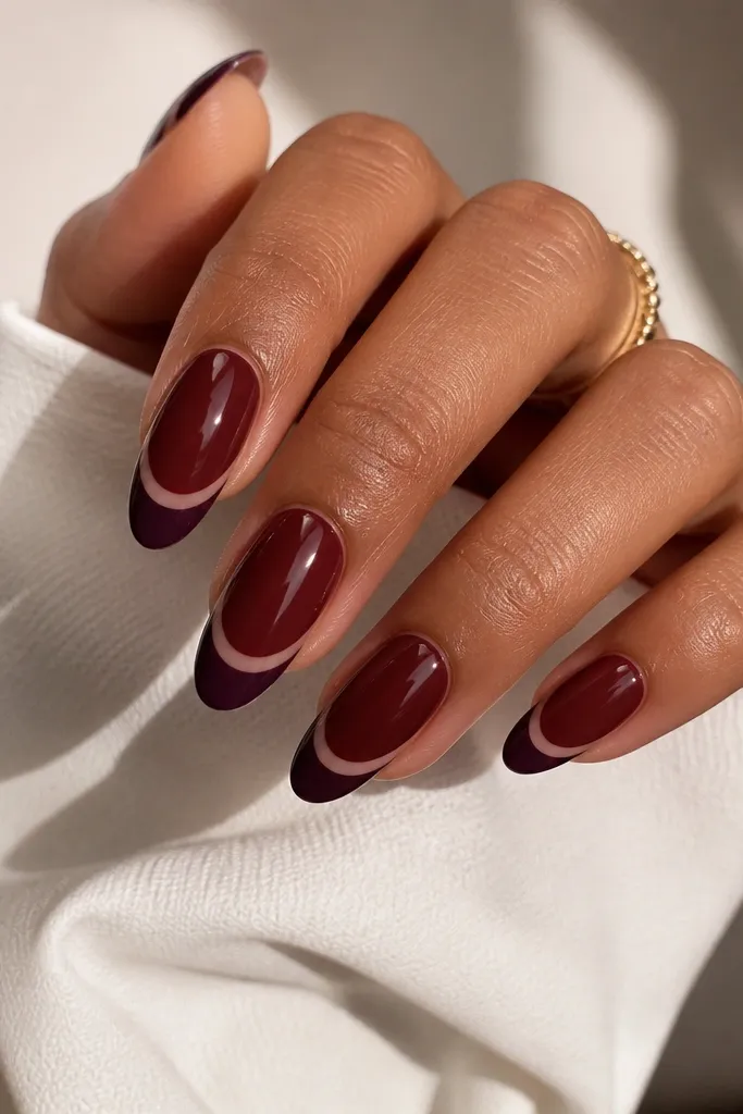 Almond nails with a dark cherry base. The French tip is a deep plum shape that leaves a small negative-space half-moon at the smile line, outlined cleanly.