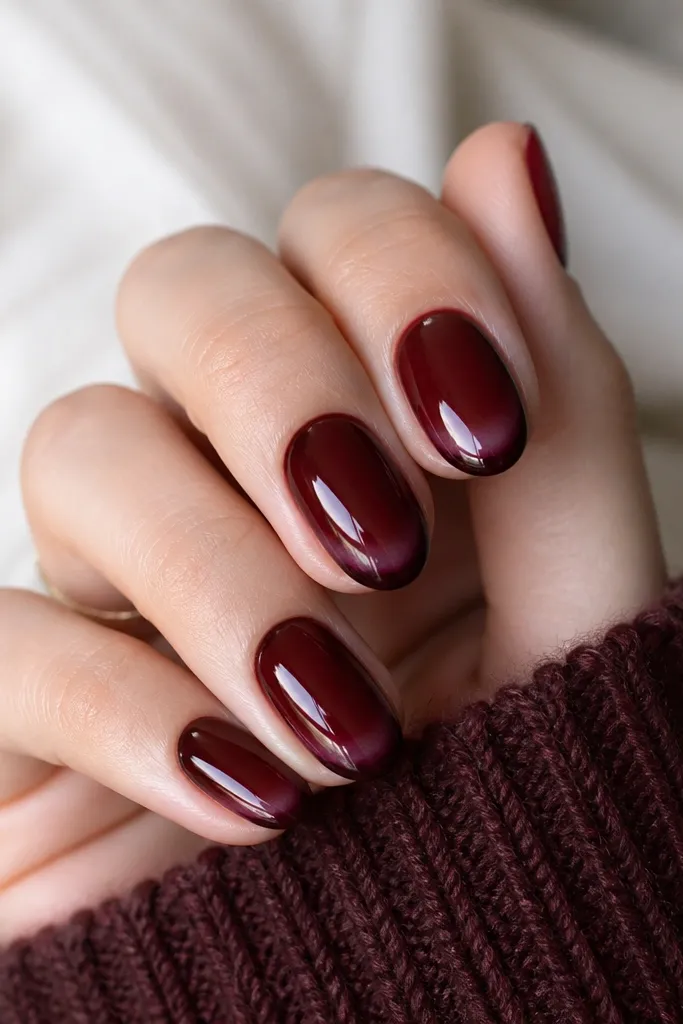 Rounded nails with glossy dark cherry base. The French tip is a curved smile line in a slightly blackened cherry shade, not white. It's painted as a soft band with a clean outer edge and a lighter inner fade toward the center of the tip.