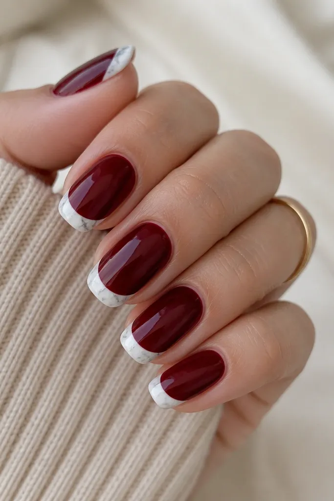 Glossy dark cherry red nails with French tips filled with a white marble pattern. The marble has thin gray veins and tiny specks, like polished stone. The outline is crisp and the marble area stops neatly at the tip curve.