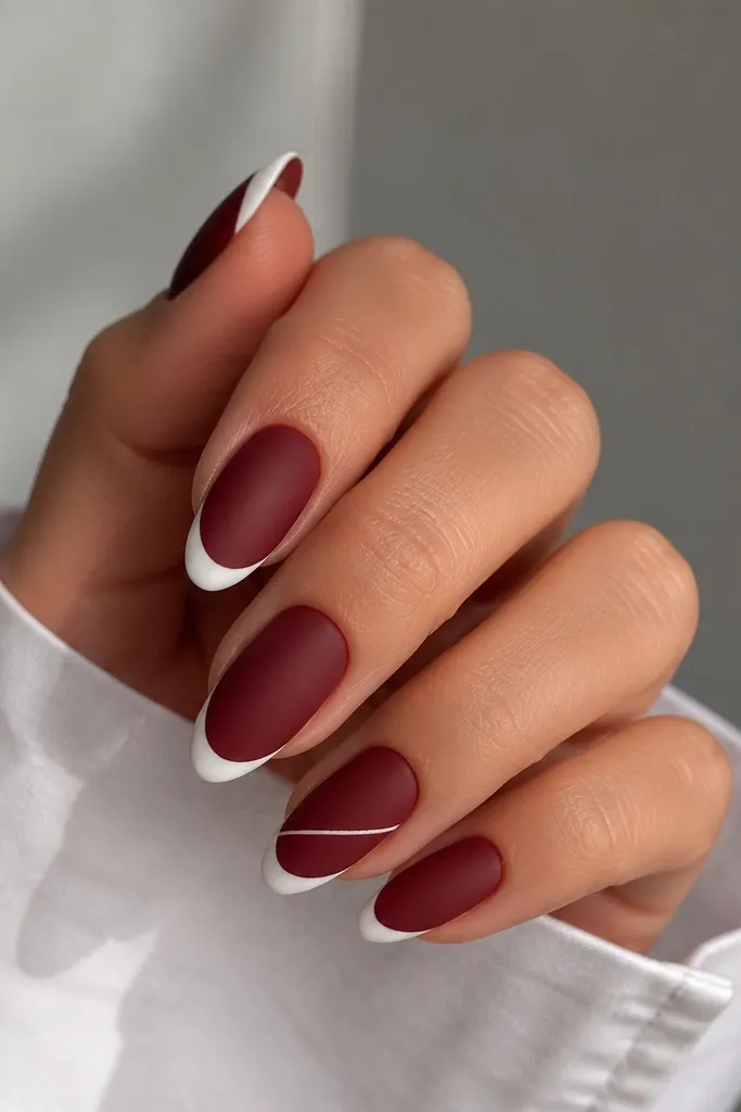 Nails are matte dark cherry red, not shiny. The French tips are glossy white in a curved shape, and one nail has a small diagonal glossy white stripe cutting across the tip area. The diagonal stripe is thin and clean.