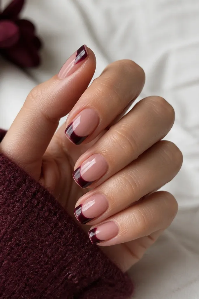 Almond nails with glossy dark cherry base. The French tip is split: the outer half is a deep plum, and the inner half is a clear or sheer nude space, separated by a thin white dividing line. The edges are crisp and straight.