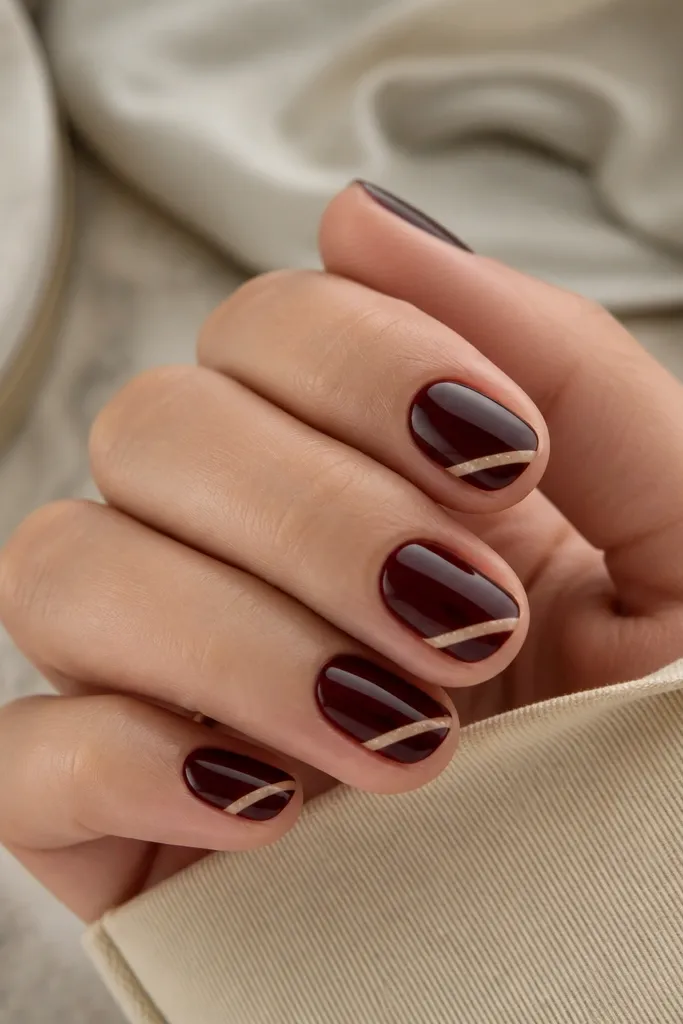 Short nails with dark cherry base; a diagonal thin nude strip crosses near the tip like a ribbon; glossy finish.