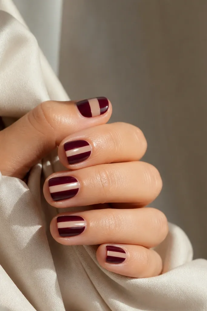 Short nails with one narrow vertical nude strip running down the center, while the rest is dark cherry red; glossy finish.