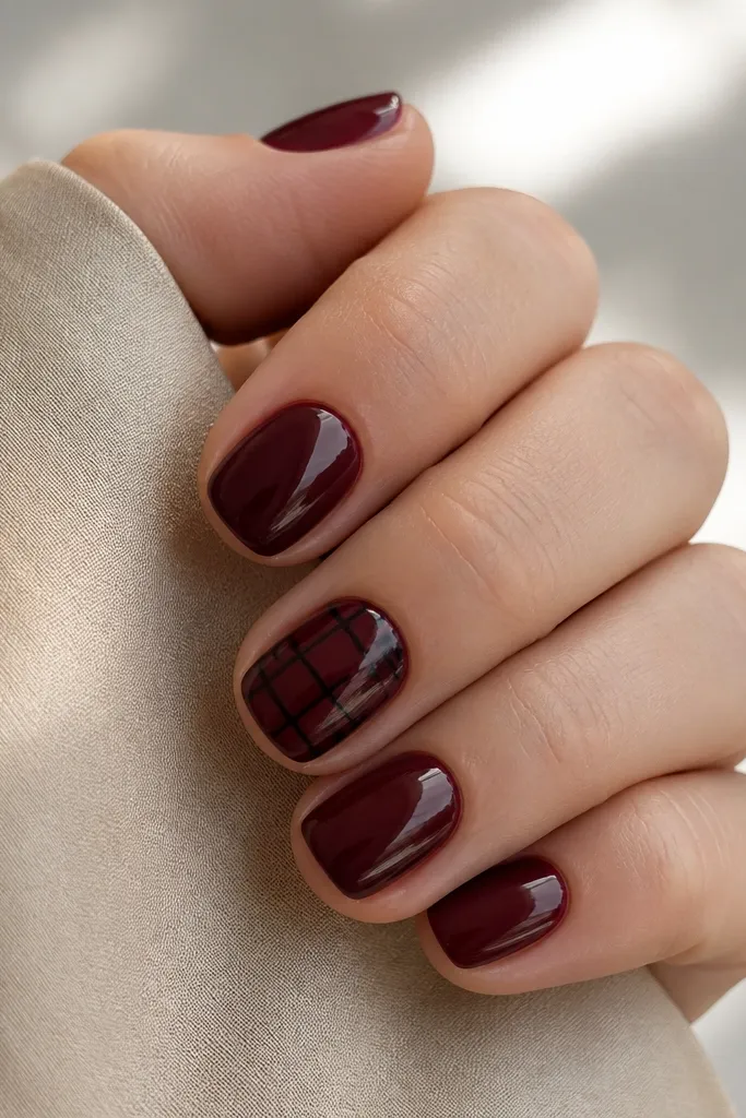 Short nails in dark cherry red with one accent nail featuring thin black crosshatch lines forming small squares in the center; glossy.
