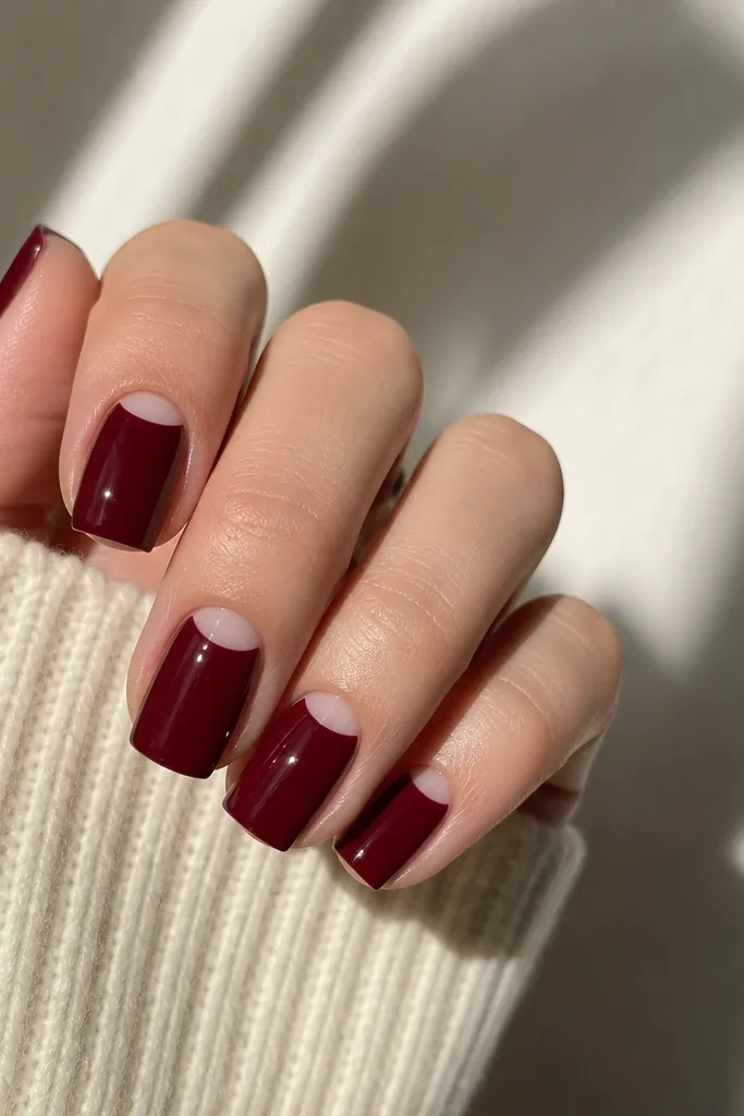 Square nails with dark cherry red polish covering most of the nail, leaving a clean half-moon gap right at the cuticle center, glossy finish.